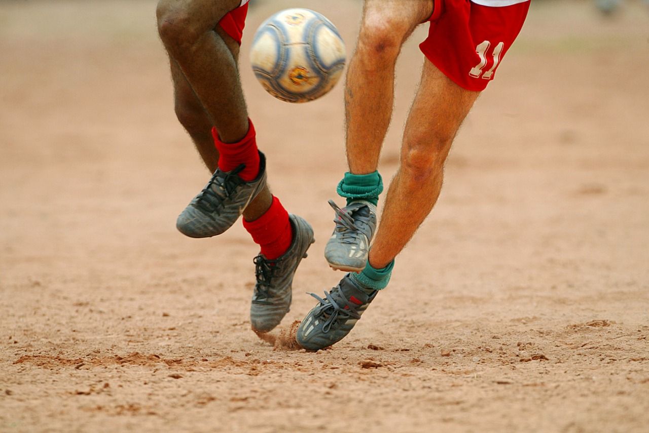 Pés de dois jogadores disputando a bola num campo de terra